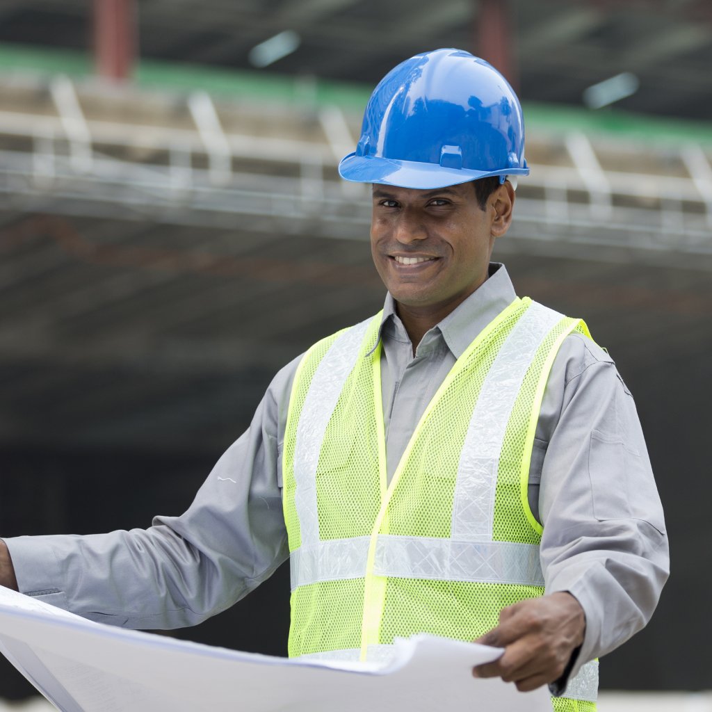Smiling worker in safety vest and helmet, is a symbol of Tharwatalwatan's Abu Dhabi Employee Protect Plan approved by the government