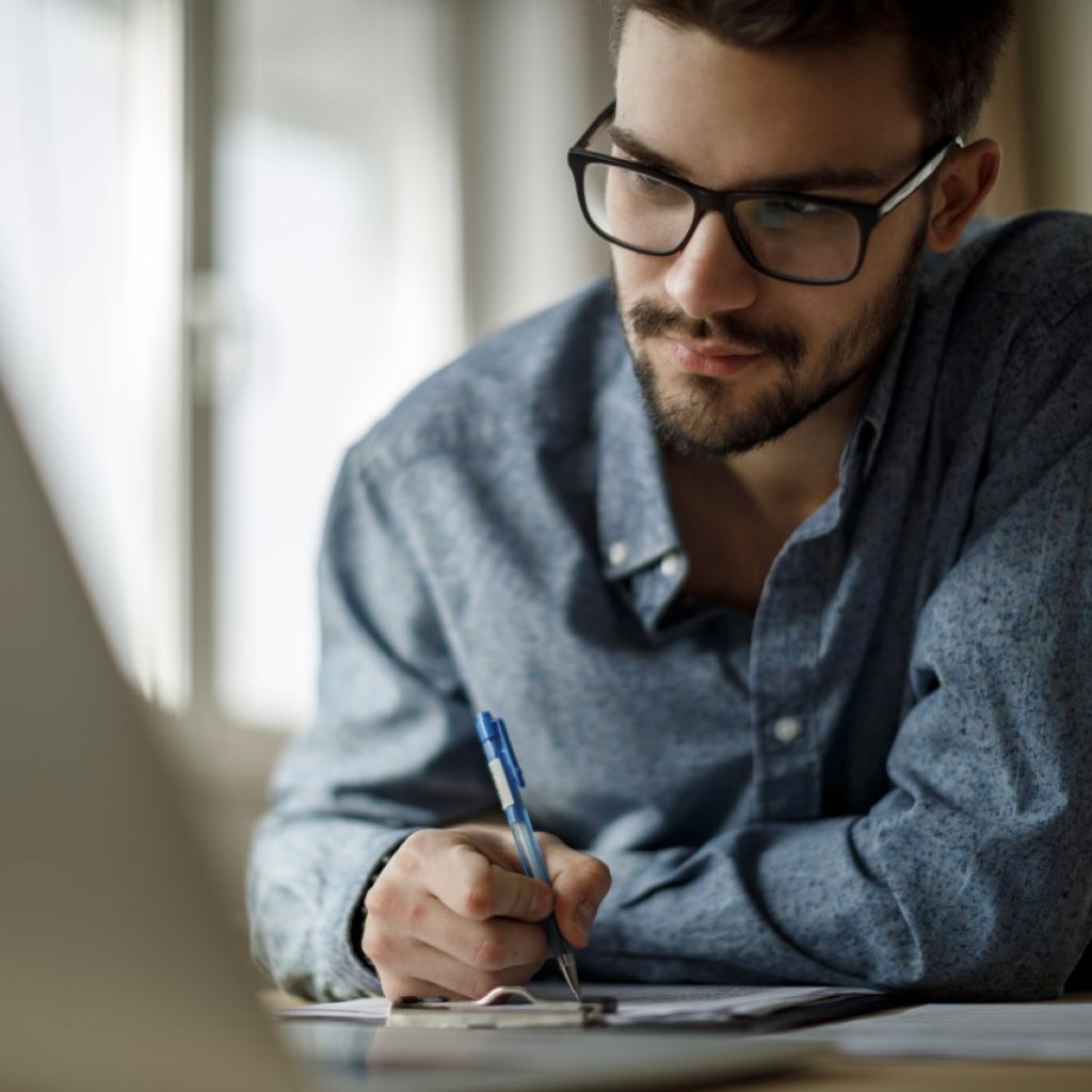 Smiling man in blue shirt seated at desk, representing Tharwatalwatan's DHA Essential Benefit Plan and customer-focused care